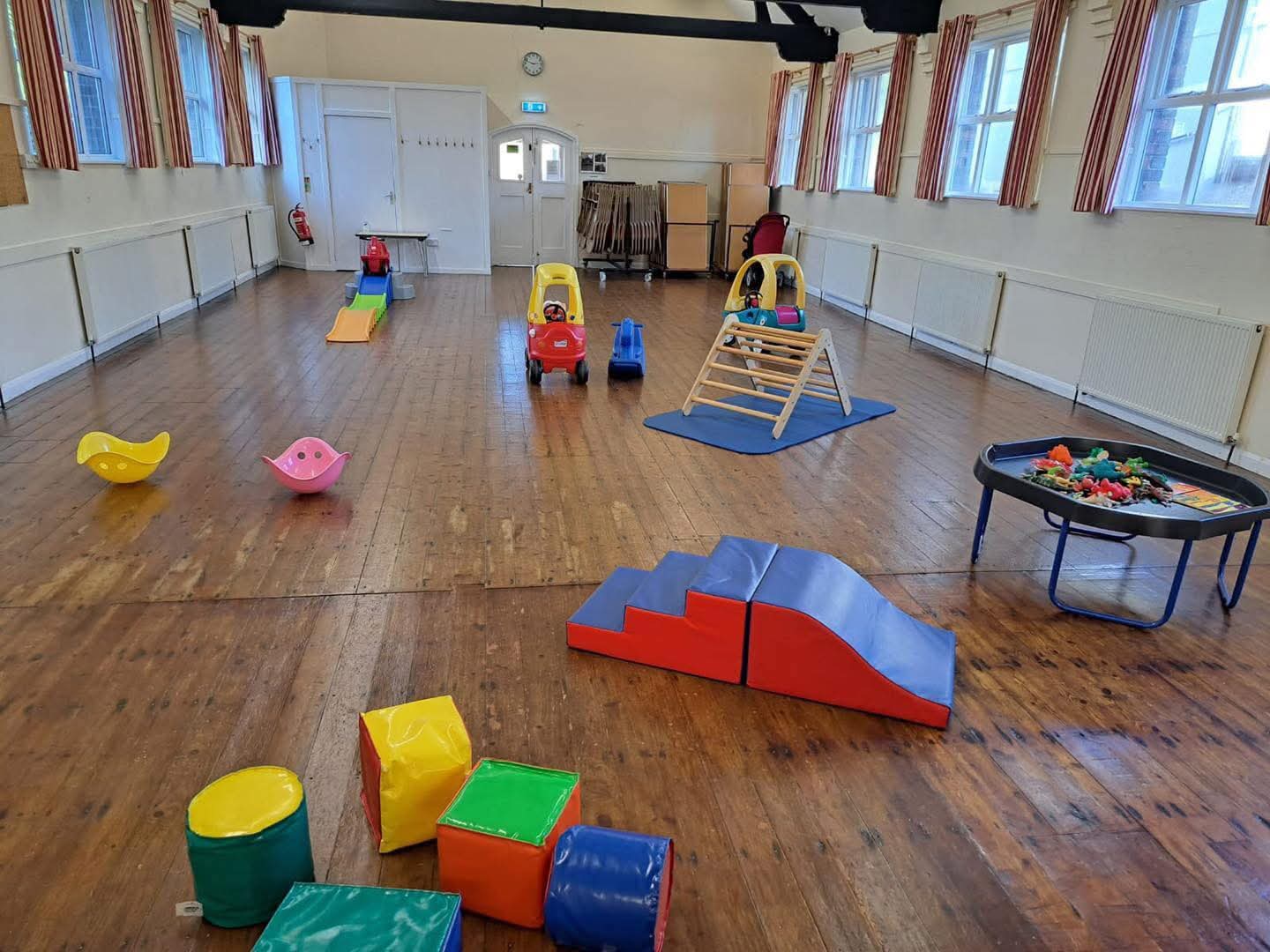 A village hall set up for Stay & Play with ride-ons, a climbing frame, soft play and a tuff tray