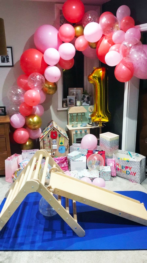 A party play zone with a wooden climbing frame and slide, balloon arch and wrapped presents