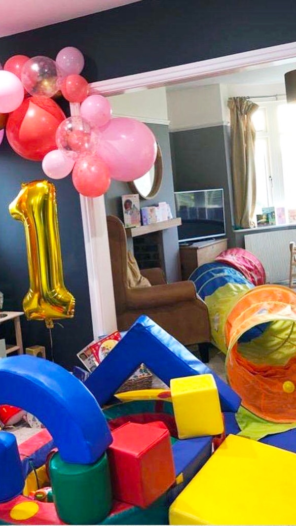 A first-birthday soft play setup at home — foam blocks, a peek-a-boo tunnel and a balloon arch