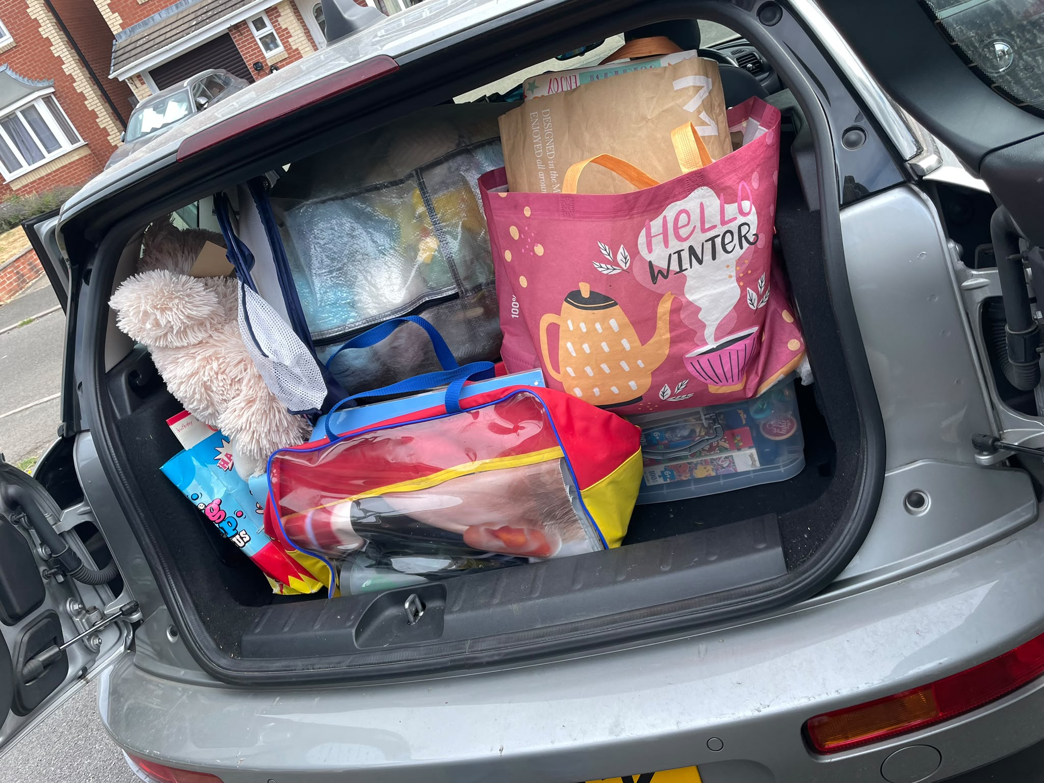 Car boot loaded with tote bags, a teddy bear and boxed games ahead of setting up the stall